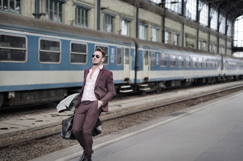 栗色西装的男人在火车旁边的人行道上行走 · 免费素材图片