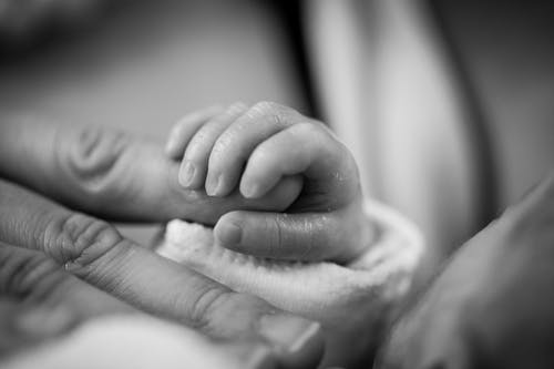 婴儿抱着手指的灰度摄影 · 免费素材图片