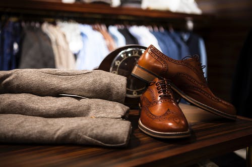 一双棕色皮革wingtip鞋子在木质表面上的灰色服装旁边 · 免费素材图片