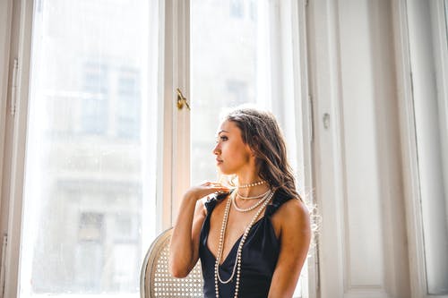 站在白色框玻璃窗旁边的黑色无袖连衣裙的女人 · 免费素材图片