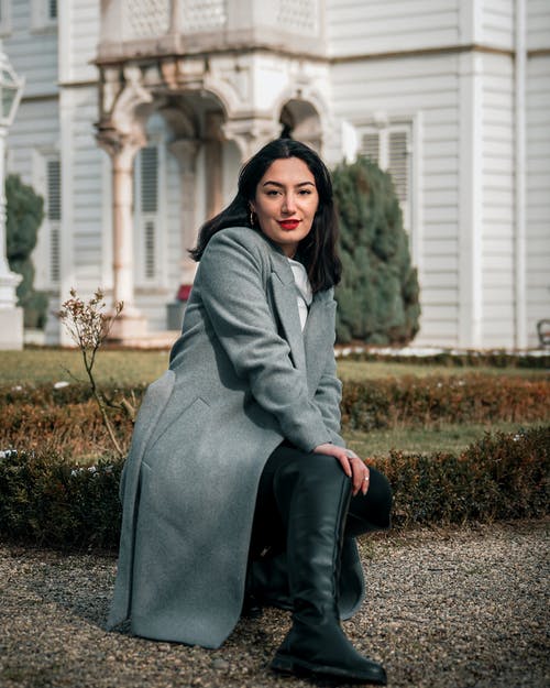 女人在灰色的外套蹲摆姿势的选择性焦点照片 · 免费素材图片