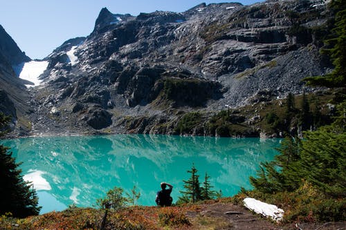 男子坐在黑岩形成包围的湖附近 · 免费素材图片