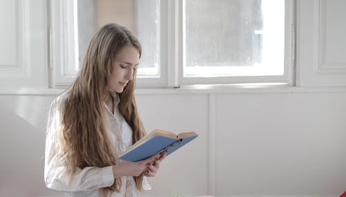 拿着蓝色书的白色长袖衬衫的女人 · 免费素材图片