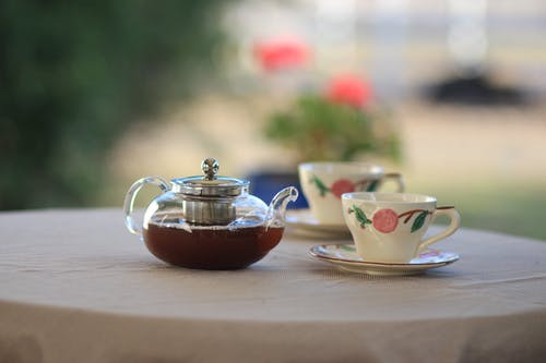 桌上选择性焦点摄影茶杯附近的透明玻璃茶壶 · 免费素材图片