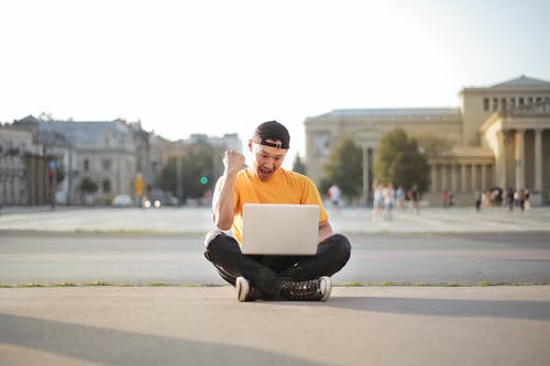 白色t恤和黑色的裤子，坐在马路上使用便携式计算机的人 · 免费素材图片