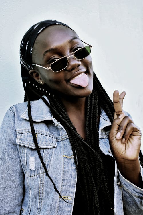 蓝色牛仔夹克穿黑色太阳镜摆和平手势时与她的舌头合影的女人的照片 · 免费素材图片