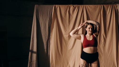 红色运动胸罩和黑色内裤站在棕色的窗帘附近的女人 · 免费素材图片
