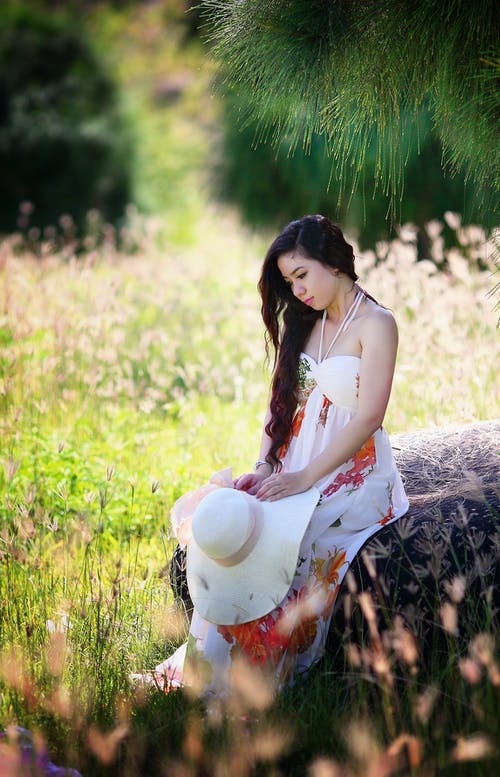 坐着的女人按住她的白色太阳帽放在她的腿上 · 免费素材图片