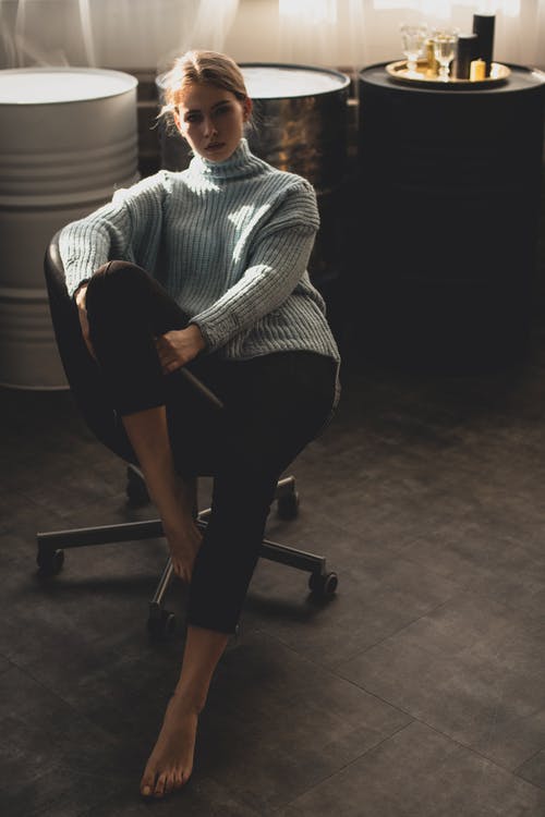 女人穿着蓝色的毛衣和黑色的裤子，坐在黑色的办公室转椅上 · 免费素材图片