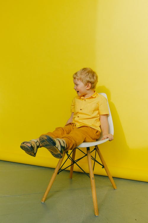 坐在椅子上墙附近的黄色polo衫的男孩 · 免费素材图片