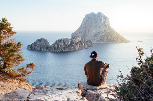 男子坐在海边岩石上的后视图 · 免费素材图片