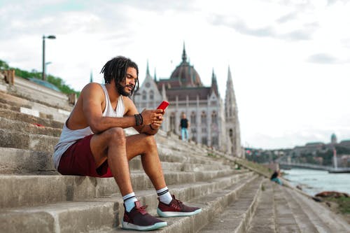 男子用他的手机坐在混凝土楼梯上 · 免费素材图片