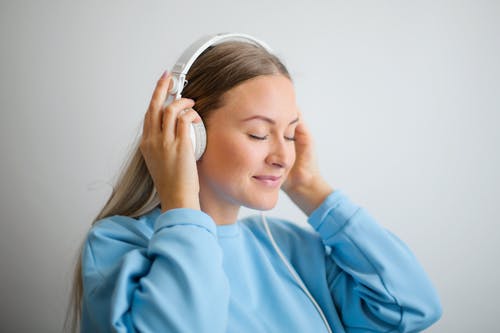 女人穿着蓝色运动衫，戴着白色耳机听音乐的肖像照片 · 免费素材图片