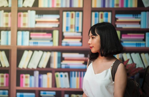 女人在书架上穿v领无袖上衣 · 免费素材图片