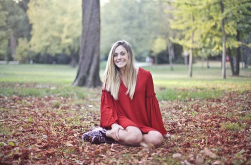 红色长袖礼服的微笑的妇女照片单独坐褐色干叶子 · 免费素材图片