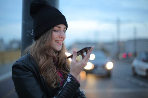 黑色的针织帽和黑色外套拿着智能手机的女人 · 免费素材图片