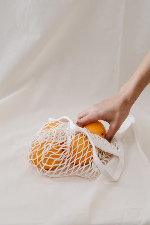 在白色的网状袋中手持橙色水果的人 · 免费素材图片
