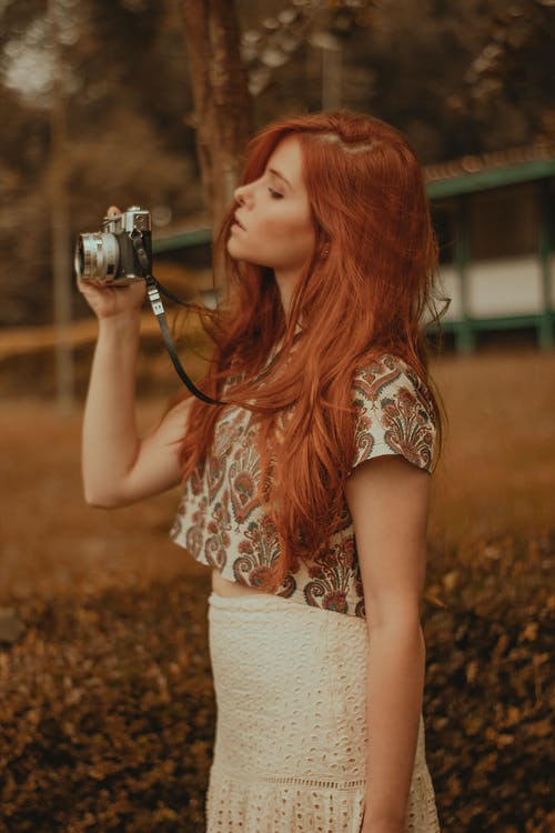拿着照相机的白色和橙色花卉无袖衫的妇女 · 免费素材图片