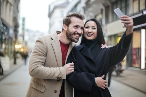 棕色外套的男人微笑着以自拍照的黑色外套的女人旁边 · 免费素材图片