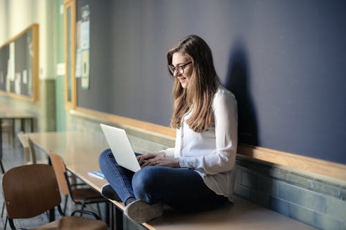 白色长袖衬衫和蓝色牛仔牛仔裤，坐在桌上，同时使用macbook的女人 · 免费素材图片