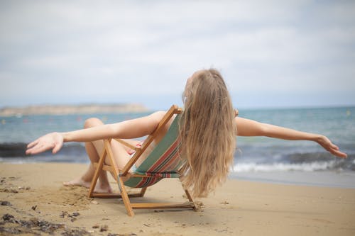 蓝色和棕色比基尼泳装的妇女坐在海滩的棕色木折叠椅 · 免费素材图片