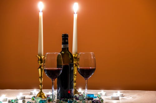 在酒瓶和点燃的蜡烛旁边的两个几乎空的长茎酒杯 · 免费素材图片