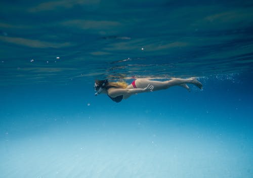 无法辨认的女士在蓝色的海洋中浮潜 · 免费素材图片