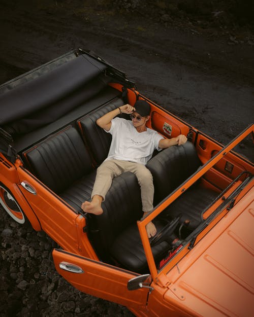 白衬衫和卡其色裤子躺在橙色车里的男人 · 免费素材图片