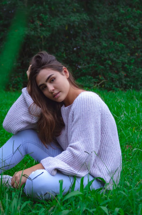 坐在绿草地上的白色针织毛衣的女人 · 免费素材图片