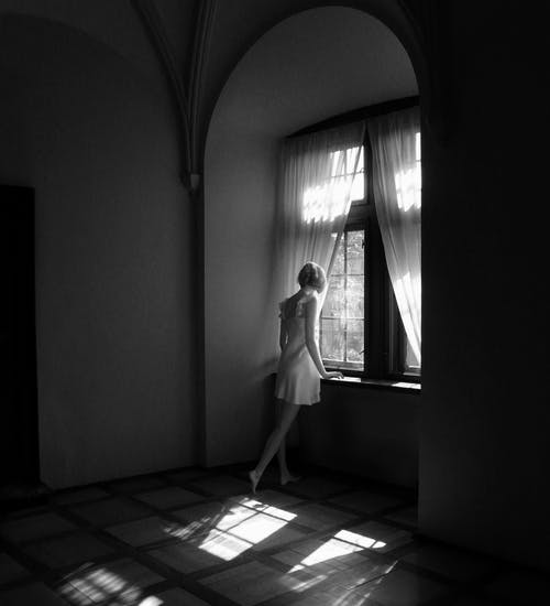 女人站在关闭的窗口旁边灰度照片 · 免费素材图片