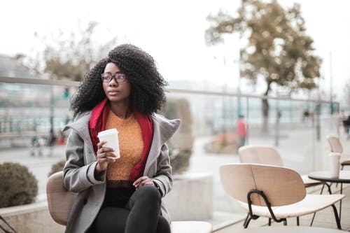 女人在灰色的外套，坐在木椅上，拿着一杯咖啡的选择性焦点照片 · 免费素材图片