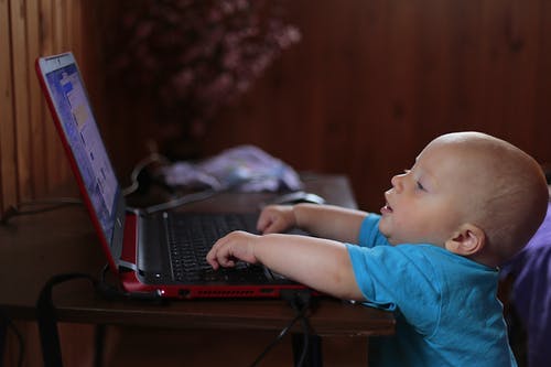 男孩在昏暗的灯光场景中使用黑色便携式计算机穿蓝色t恤 · 免费素材图片