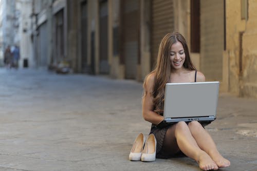使用笔记本电脑时坐在地板上的女人 · 免费素材图片