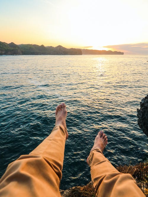 穿着黄色的裤子，坐在被海包围的岩石上的人 · 免费素材图片
