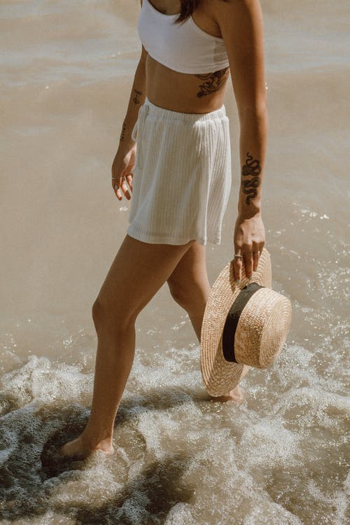 白色和蓝色条纹裙子和棕色太阳帽站在水上的女人 · 免费素材图片