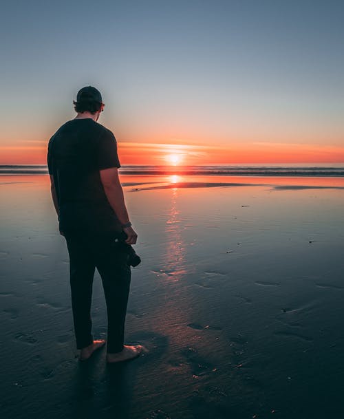 在日落时站在海滩上的男人 · 免费素材图片