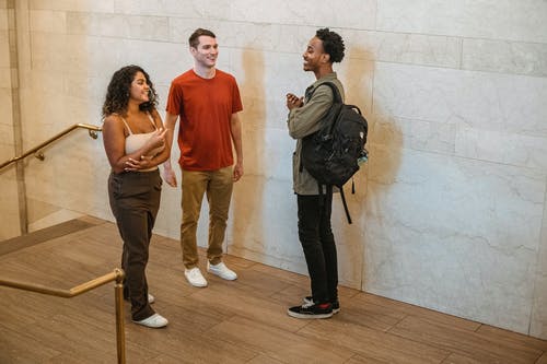 橙色背心和蓝色牛仔牛仔裤站在灰色夹克的女人旁边的女人 · 免费素材图片