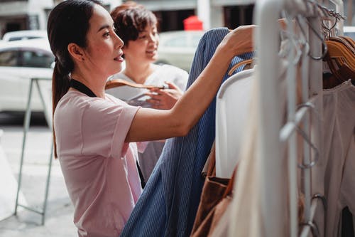 亚洲买家在街边商店的架子上选择衣服 · 免费素材图片