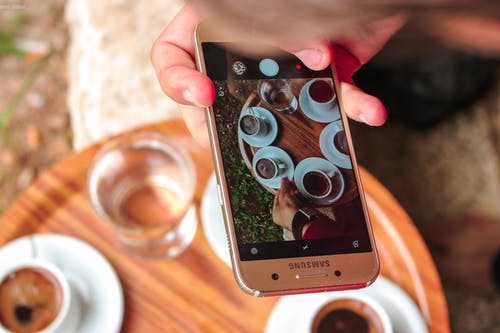 拿着三星galaxy智能手机在咖啡上拍照的人 · 免费素材图片
