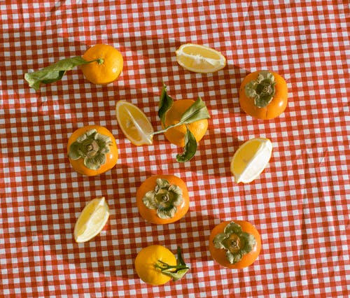 成熟的柑橘和柿子放在红色方格桌布上 · 免费素材图片