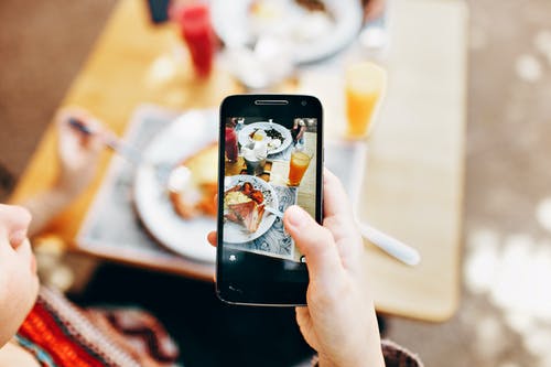拿着电话的人拍被服务的食物的照片 · 免费素材图片