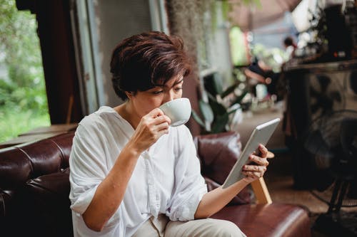 严重的亚裔女子浏览平板电脑和喝咖啡 · 免费素材图片