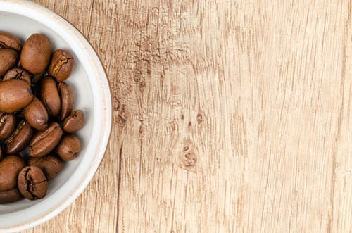 棕色木制表面上的白色陶瓷碗上的咖啡豆 · 免费素材图片