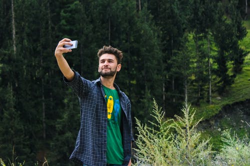 蓝色运动衫和绿色上衣以自拍照附近绿树的男人 · 免费素材图片