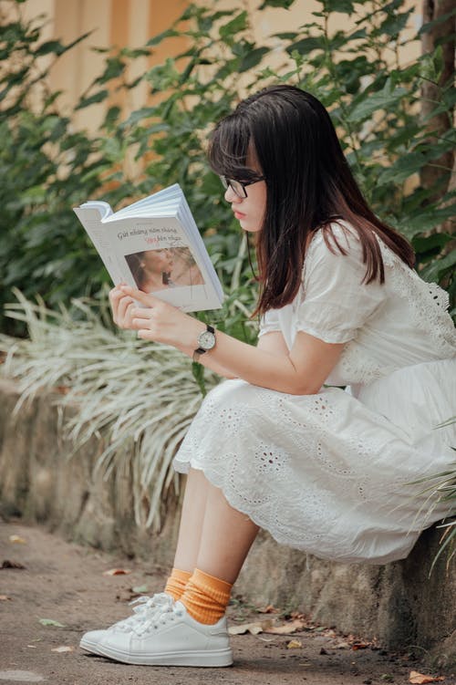 女人坐在灰色的混凝土砌块看书 · 免费素材图片
