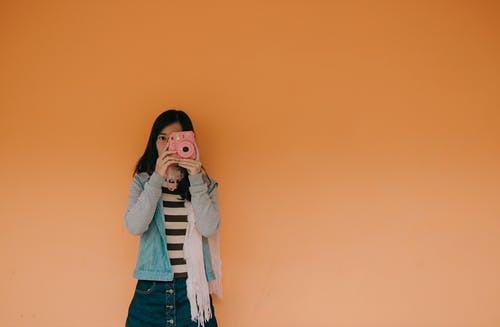 拿着桃红色fujifilm Instax照相机的蓝夹克的妇女 · 免费素材图片