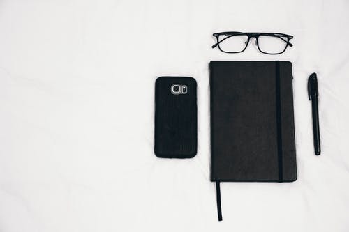 规划器旁边的黑色智能手机，眼镜和笔 · 免费素材图片