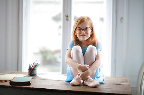 玻璃的愉快的逗人喜爱的小女孩坐在轻的客厅的桌上 · 免费素材图片