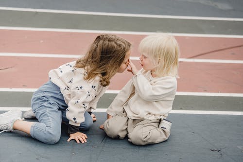 2个女孩坐在灰色的水泥地板上 · 免费素材图片