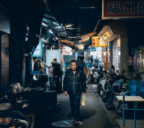 晚上在建筑物之间的人行道上行走的成熟亚洲人 · 免费素材图片